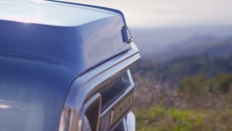 closeup of the front of a blue pickup truck as it drives along a rural road