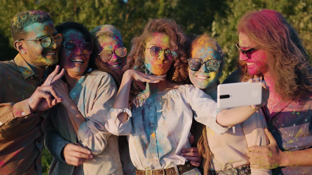 Slow motion of smiling young people dirty with bright paint taking selfie in park using smartphone camera