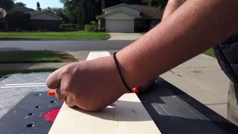 white male marking wood board with a tape measure in the day