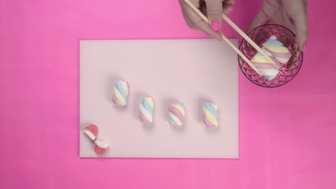 Mani che dispongono marshmallow colorati con le bacchette su sfondo rosa