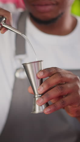 barman pours liqueur into jigger in club closeup. black bartender prepares alcohol ingredient for cocktail in bar. young man makes drink at counter