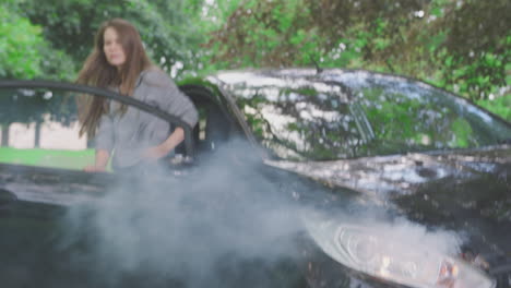 woman getting out of smoking car and inspecting accident damage before calling emergency services