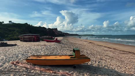 hermoso paisaje de mano de un pequeño barco amarillo atracado en la playa de amor tropical en paraíba, brasil con arena dorada, agua turquesa y cielos nublados azules en un cálido día soleado de verano