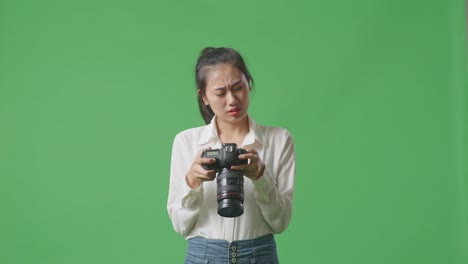 asian photographer looking at the pictures in the camera then having a headache while standing on green screen background in the studio