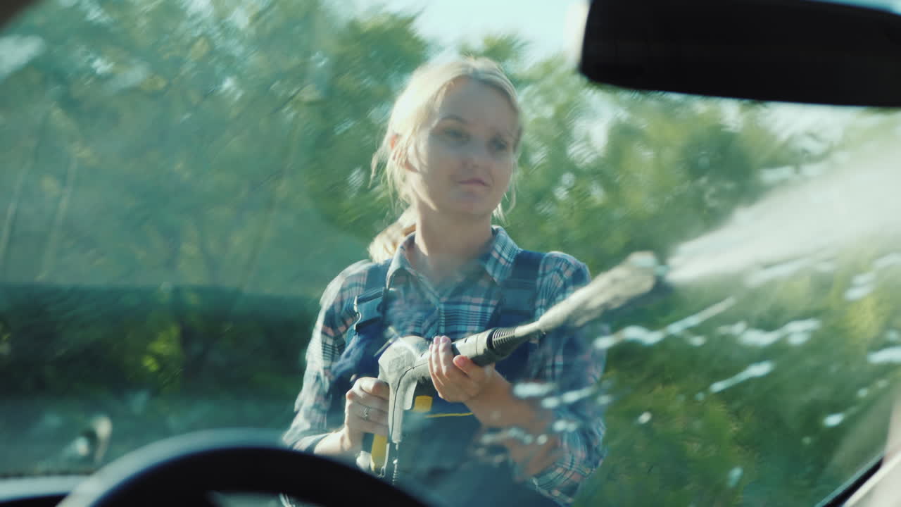 Vista interna di un'auto: una donna lava la sua auto con un'idropulitrice