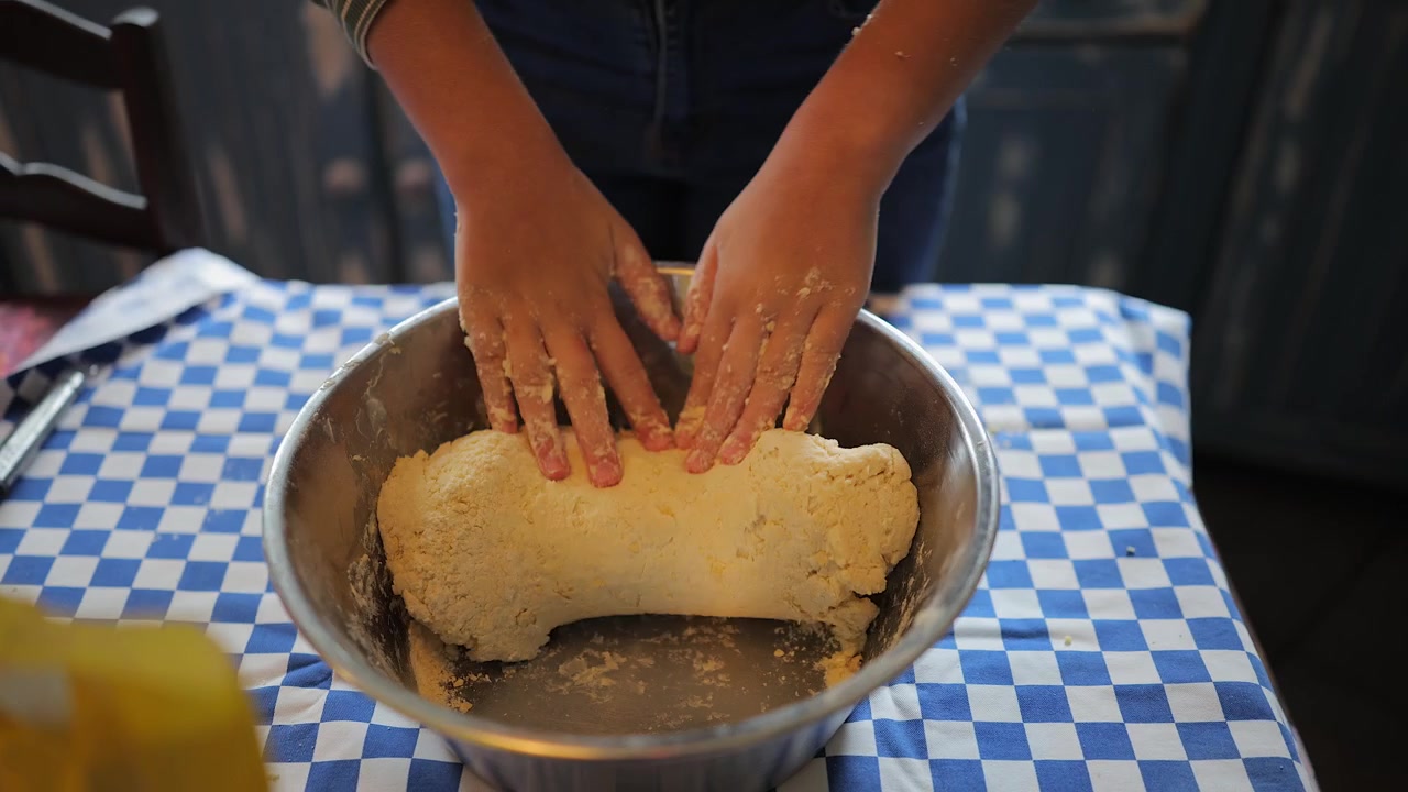 Menina amassa a massa em uma tigela de aço inoxidável ao fazer pãezinhos de canela em casa.