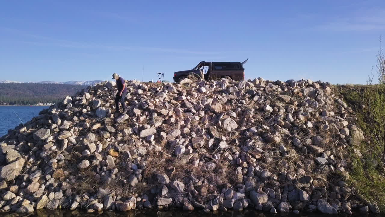 Aerial shot of a man standing on rocky shore during fishing trip, ready to cast