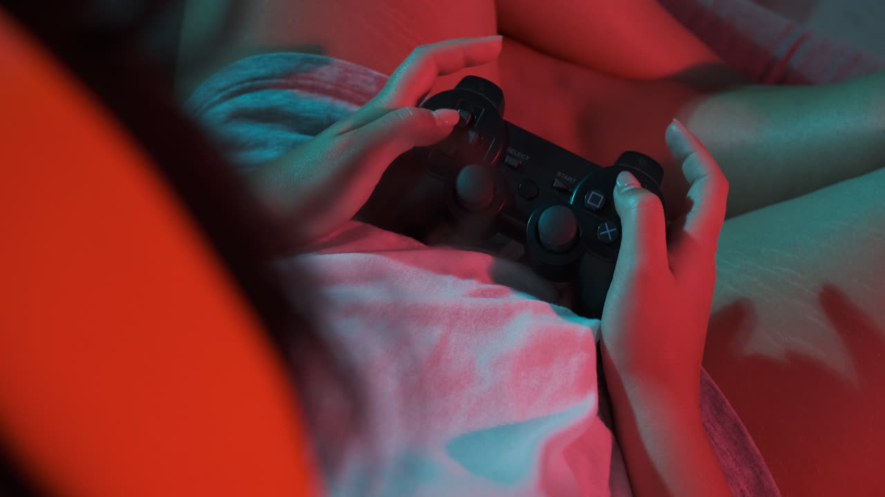 Close-up of women's hands with a game console controller while playing. Colorful lights
