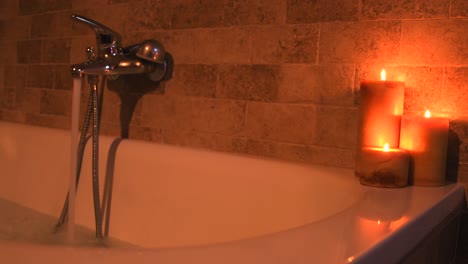 Hot-water-filling-up-a-home-spa-bathtub,-for-self-care,-next-to-some-candles