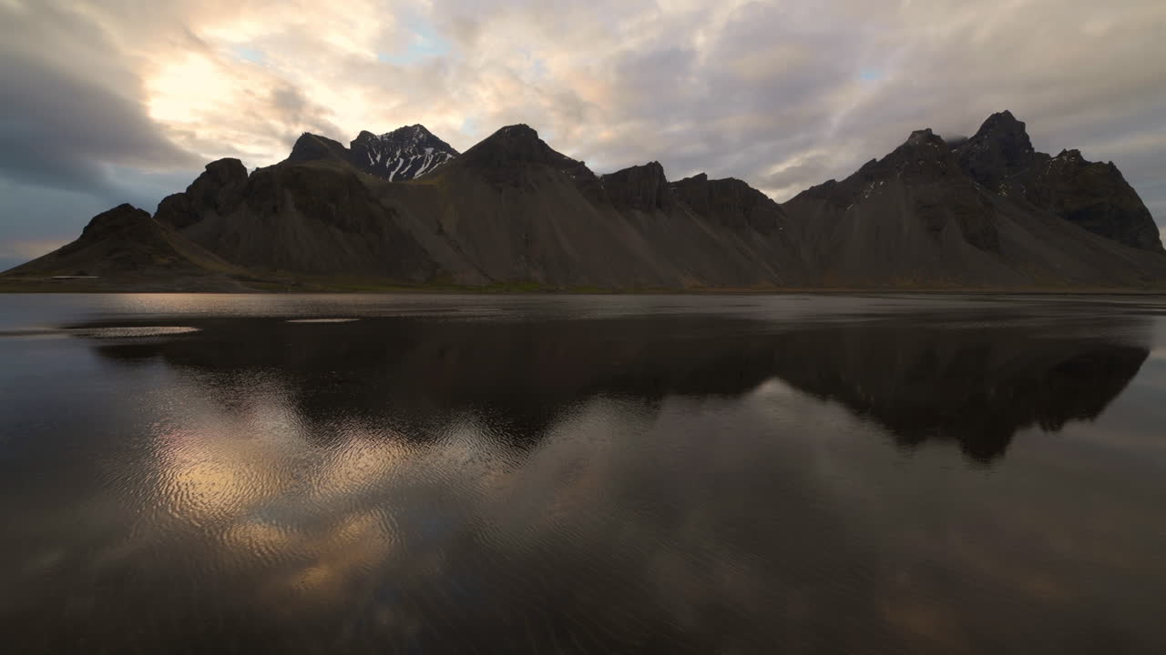 reflexiones de la montaña vestrahorn en aguas tranquilas y cielo nocturno nublado con rayos del sol