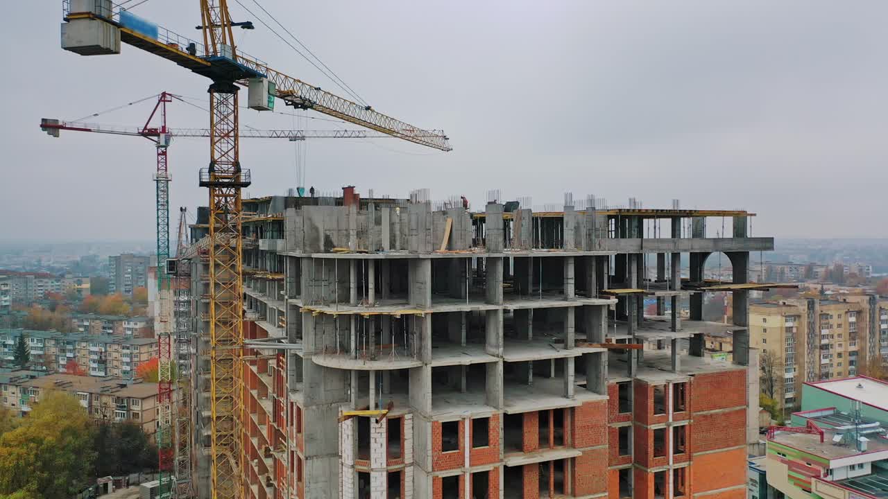 New construction site in the city. Two big cranes constructing the urban building. Construction of high-rise building on the city background. Aerial view. Round motion of camera.