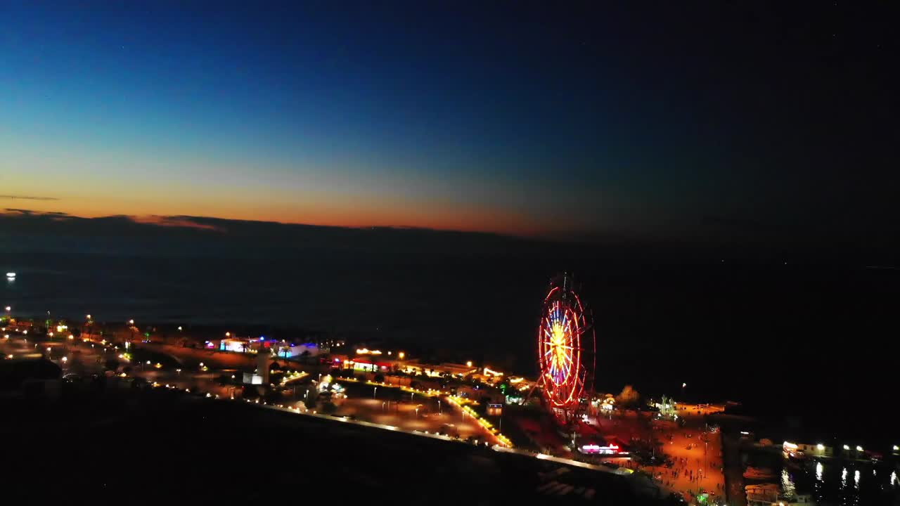 BATUMI, GEORGIA, July 5th, 2021: Ferris Wheel Lights at Night with sea background. Neon colored lights flashing on the Ferris wheel. Embankment of Batumi, Georgia.