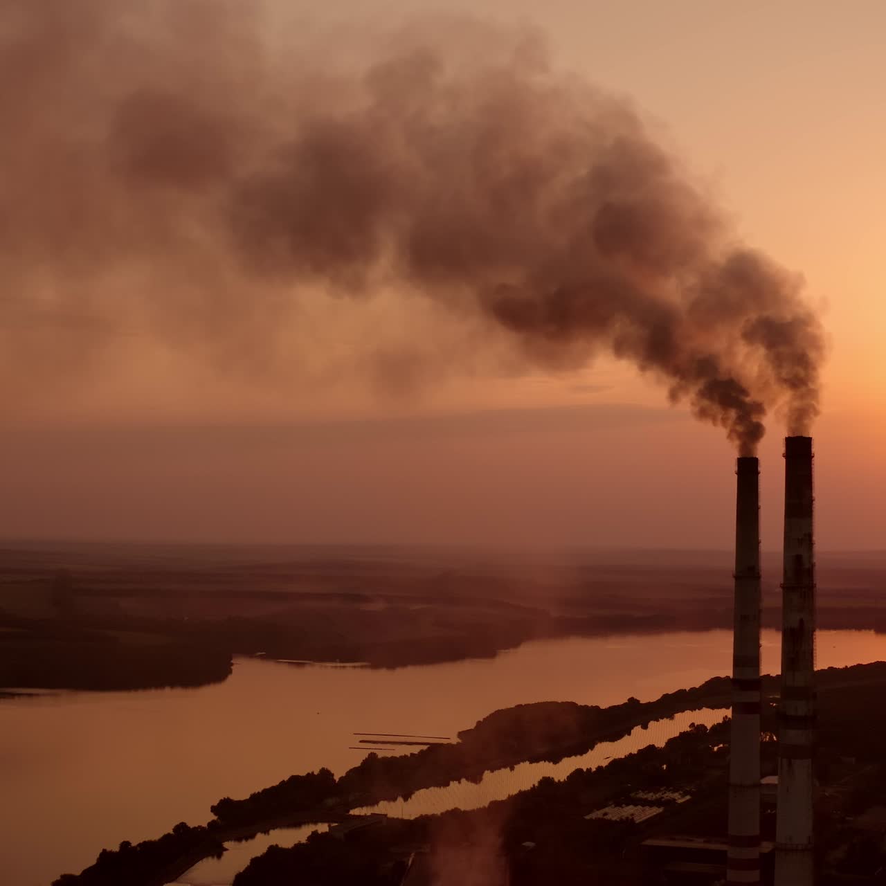 Dangerous fumes from industry pollute the air. Harmful factory with smoking pipes near river at sunset. Global warming. Environmental pollution