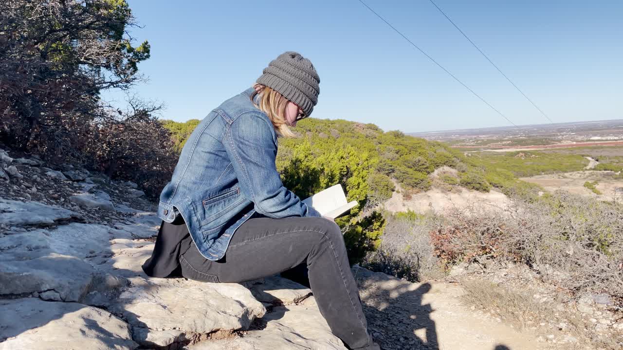 girl reading a book on a mountain overlooking the view