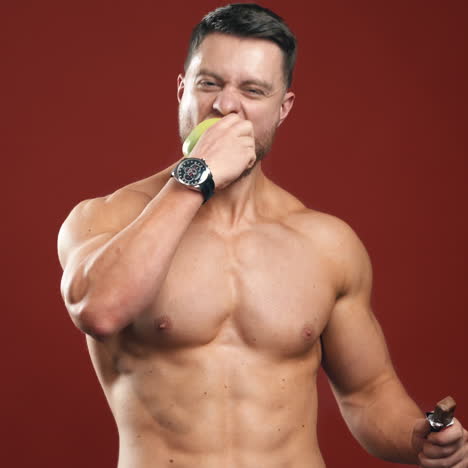 shirtless bodybuilder eating apple. portrait of a handsome man with muscular body chooses fresh fruit instead chocolate bar. smiling strong male eating vitamins in studio.