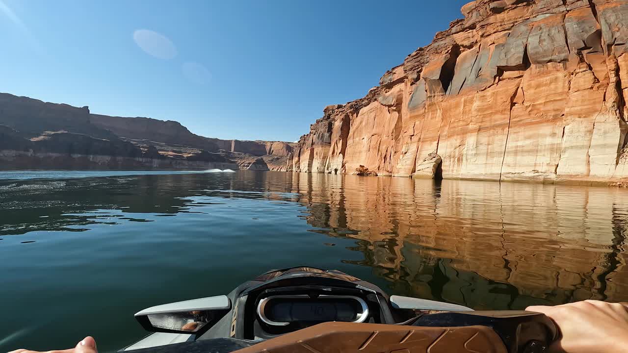 POV d'un jet ski naviguant sur le lac Powell près de falaises de grès par une journée de ciel bleu.