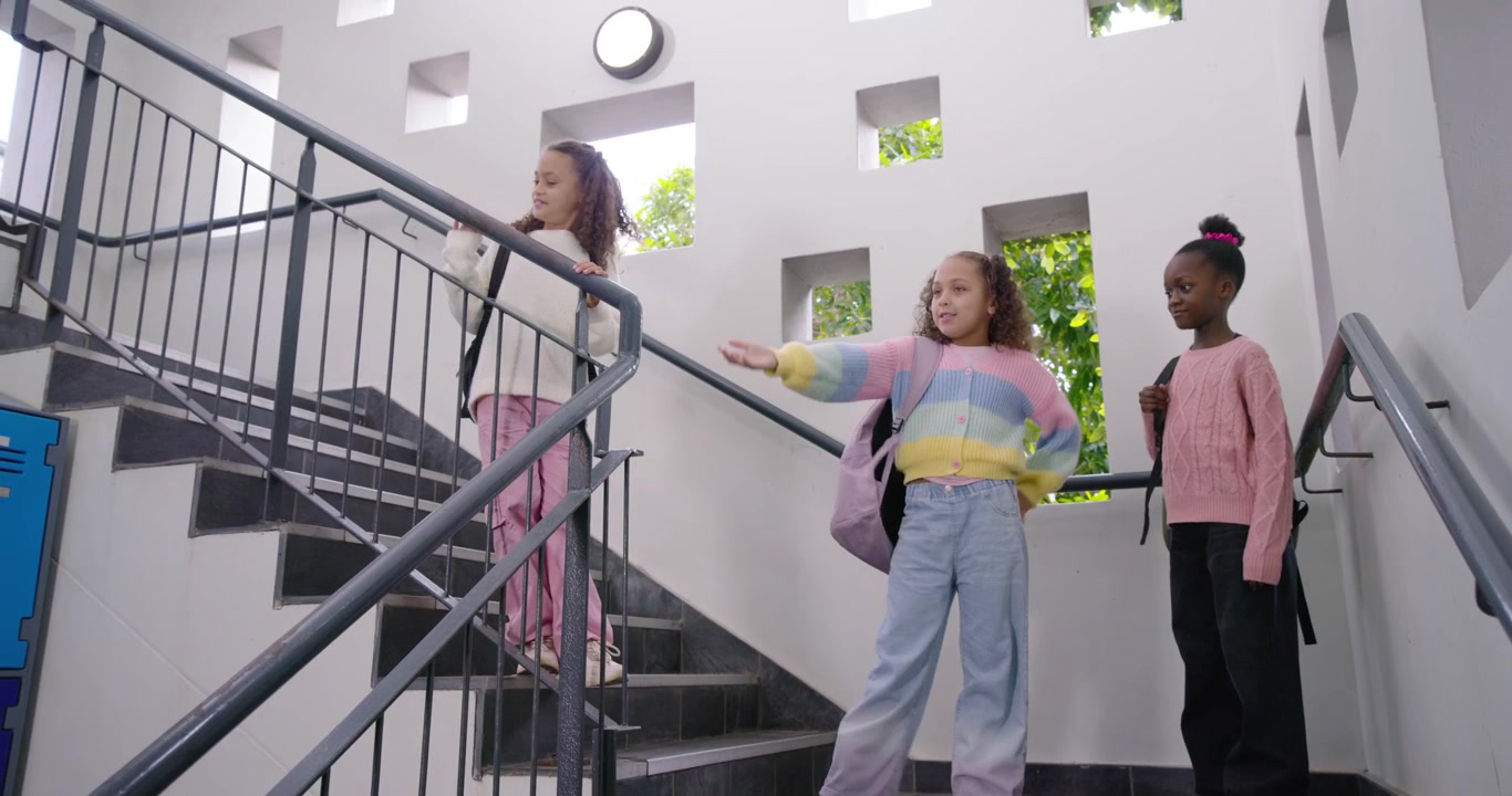 Tre afrikanske piger kommer ind fra venstre på skoletrappen, klatrer, gestikulerer og bevæger sig med rygsække.