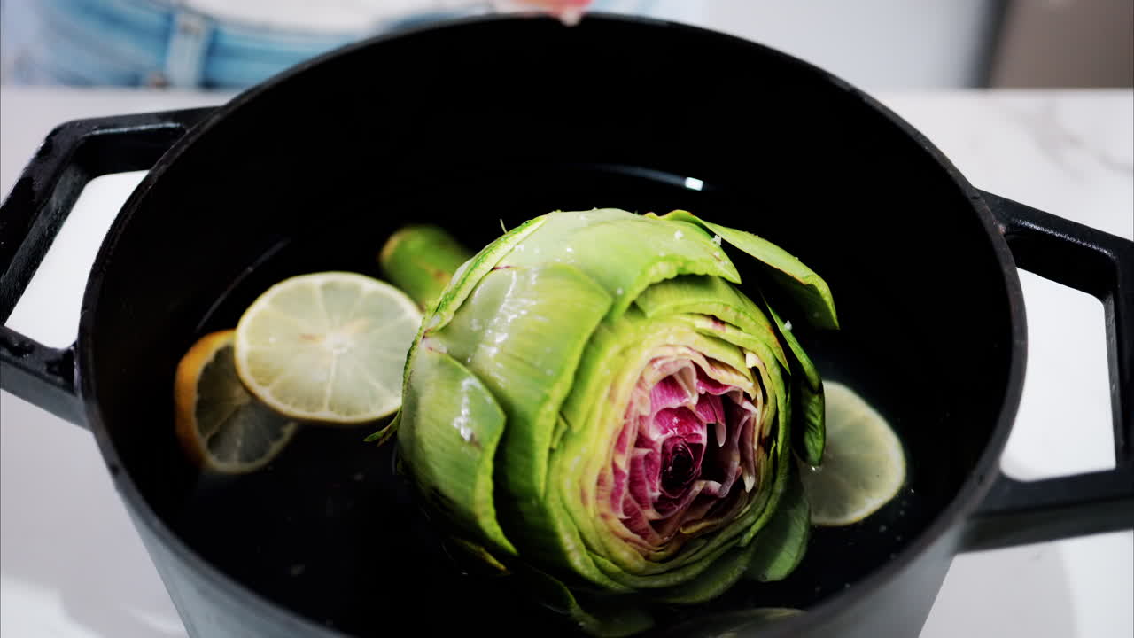 Woman pouring salt over an artichoke in a pot with water and lemons