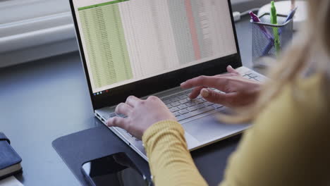 Midsection-of-biracial-woman-sitting-at-desk-using-laptop-at-home,-slow-motion