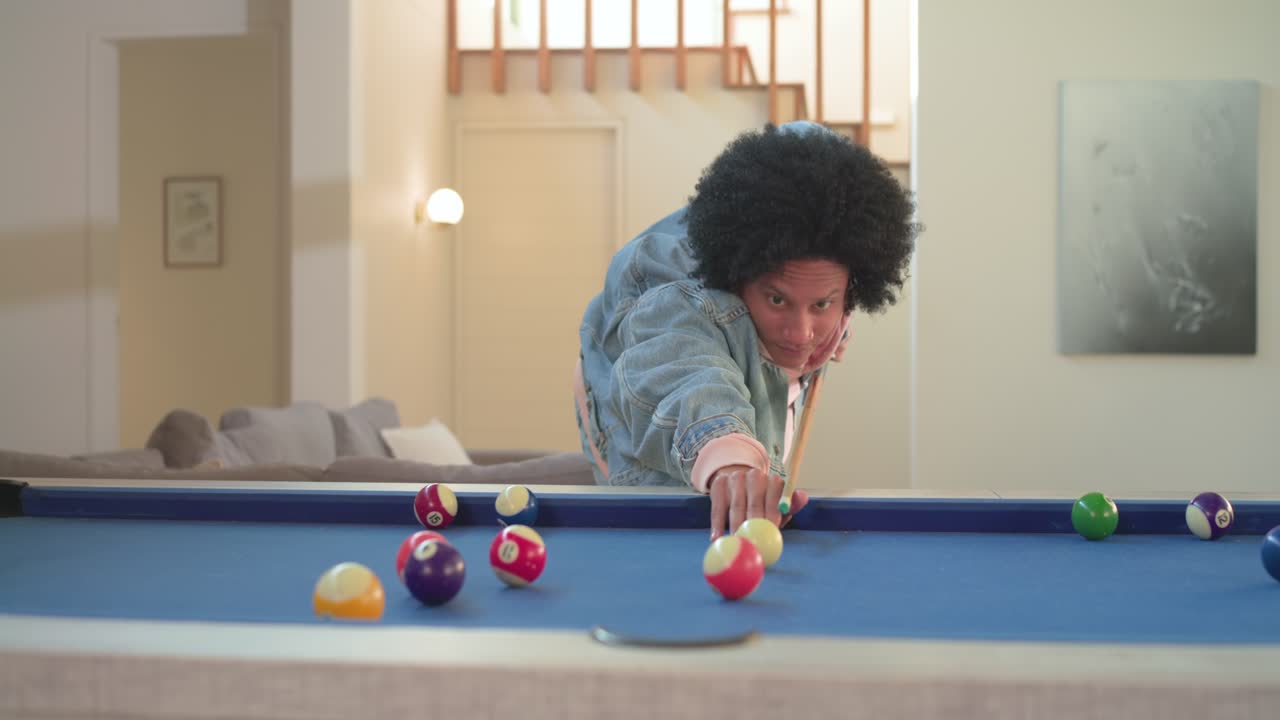 Depois de se preparar para o lance, homem afro-americano acertando a bola de bilhar em casa, comemorando