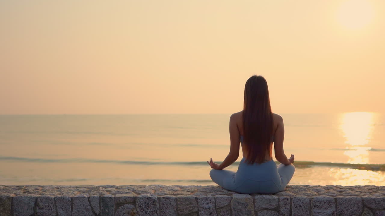 Young sports girl meditates at sunset, calm ocean sea, long hair