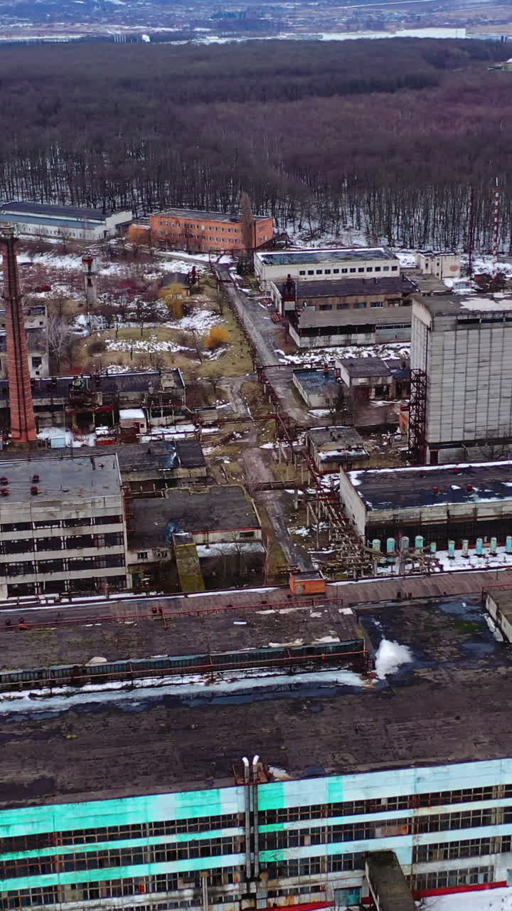 Empty broken industrial plant. Old factory near the forest. Flight over the ruined place after the military actions. Aerial view. Vertical video