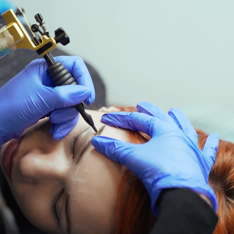 the process of applying permanent makeup on the client's eyebrows in a beauty salon using professional equipment. close-up