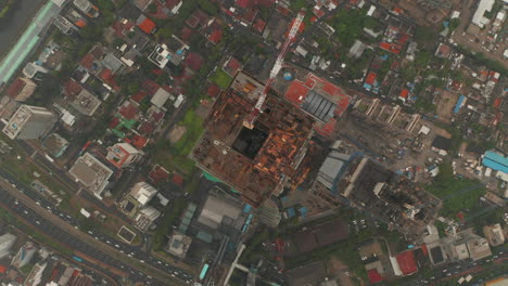 Aerial-Birds-Eye-Overhead-Top-Down-View-descending-towards-the-top-of-the-skyscraper-under-construction-in-busy-city-center