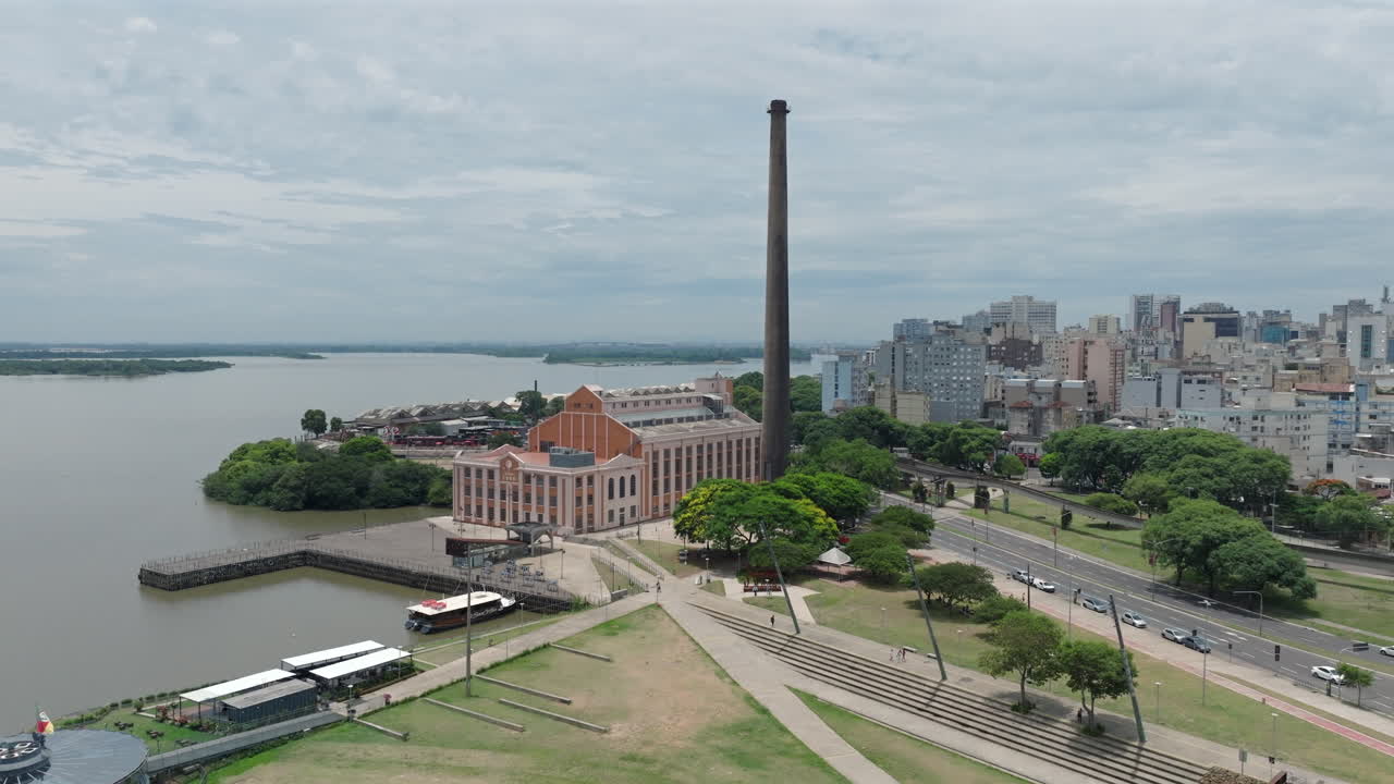 Usina do Gasometro di Porto Alegre yang diabadikan dalam orbit mundur udara sinematik terungkap. Menampilkan jalan tepi laut dan pemandangan kota di bawah langit mendung. Direkam dalam video 4K D-Log profesional 10-bit