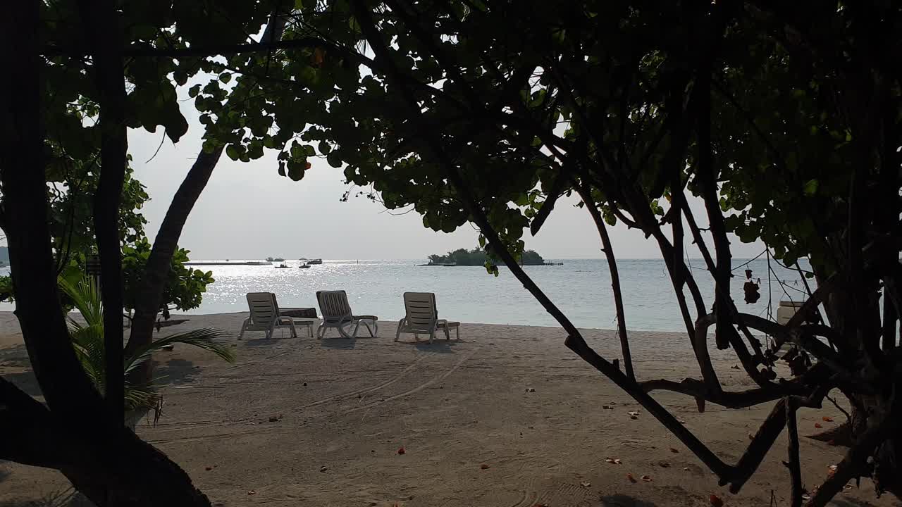 Static shot of beach chairs on seashore and boat in Maldives