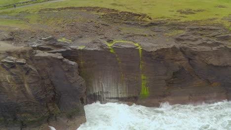 aerial dynamic shot captures the sharp edges of the cliffs of moher battered by a rough atlantic ocean. doolin