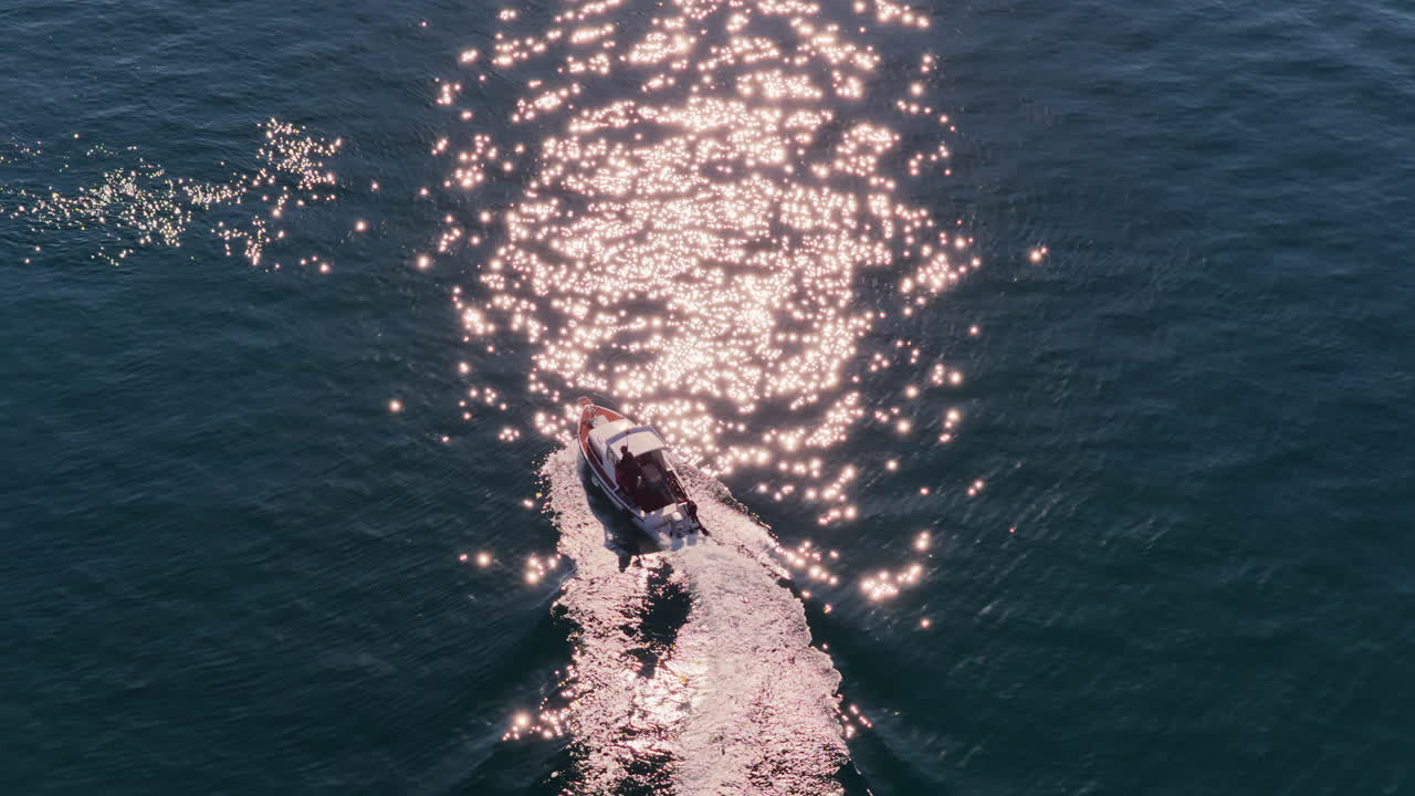Aerial drone view of a small motorboat speeding across the water, leaving a white foamy trail behind it on the calm turquoise sea. Biograd na Moru, Croatia