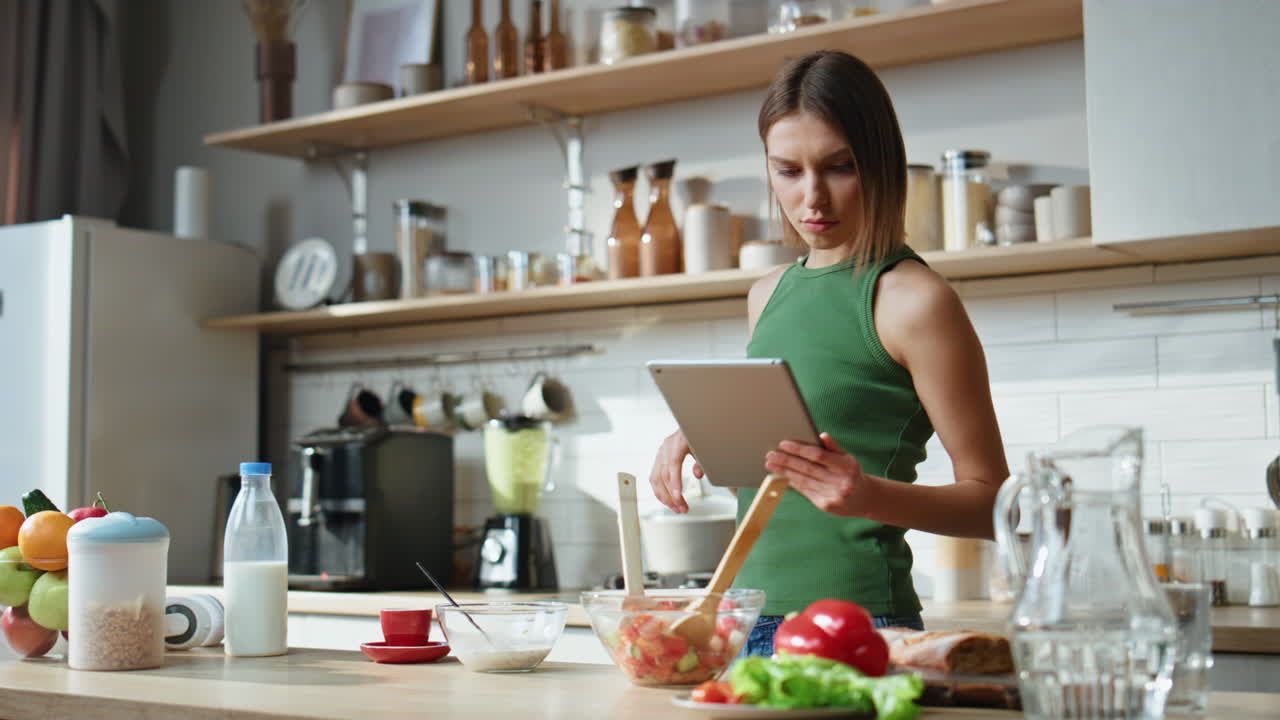 Woman Using Tablet in Kitchen While Preparing Food