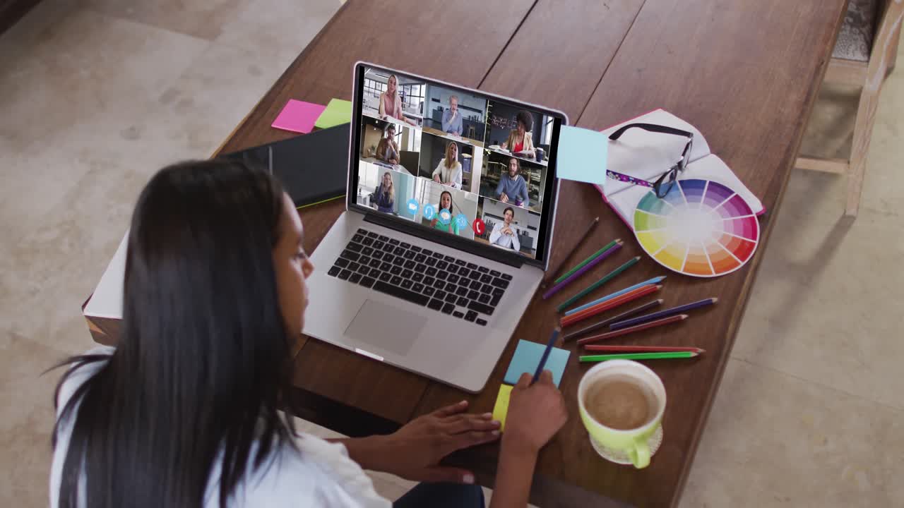 Mujer caucásica usando laptop en videollamada con colegas y tomando notas
