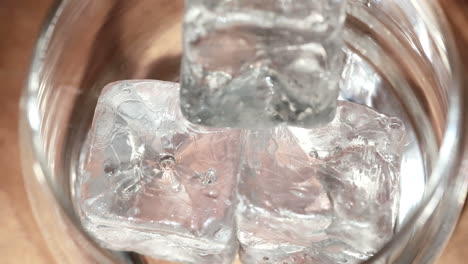 tongs placing ice into tumbler and whiskey being poured over