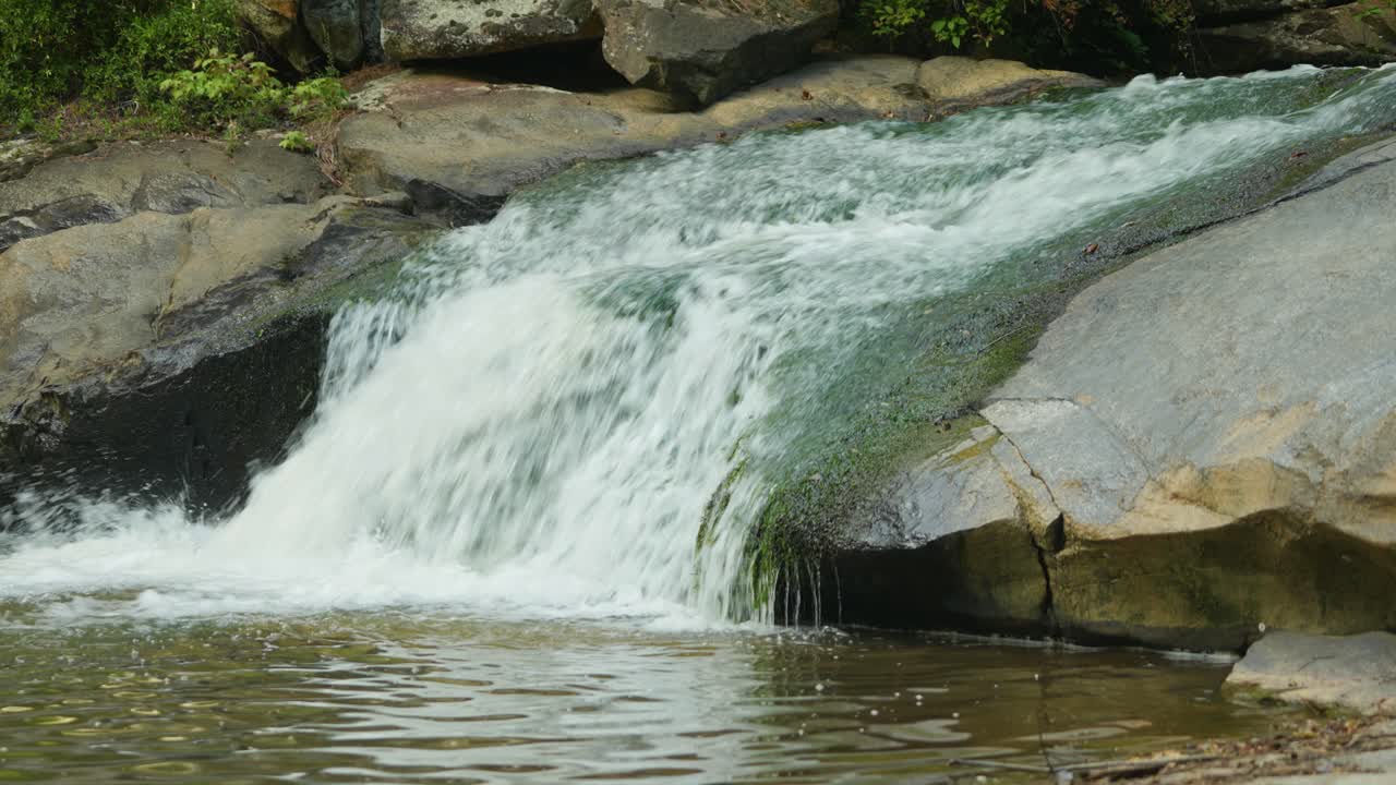 una corriente de rápido movimiento rueda desde un saliente rocoso hacia una gran masa de agua