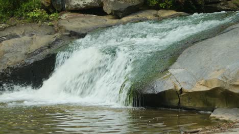 Una-Corriente-De-Rápido-Movimiento-Rueda-Desde-Un-Saliente-Rocoso-Hacia-Una-Gran-Masa-De-Agua