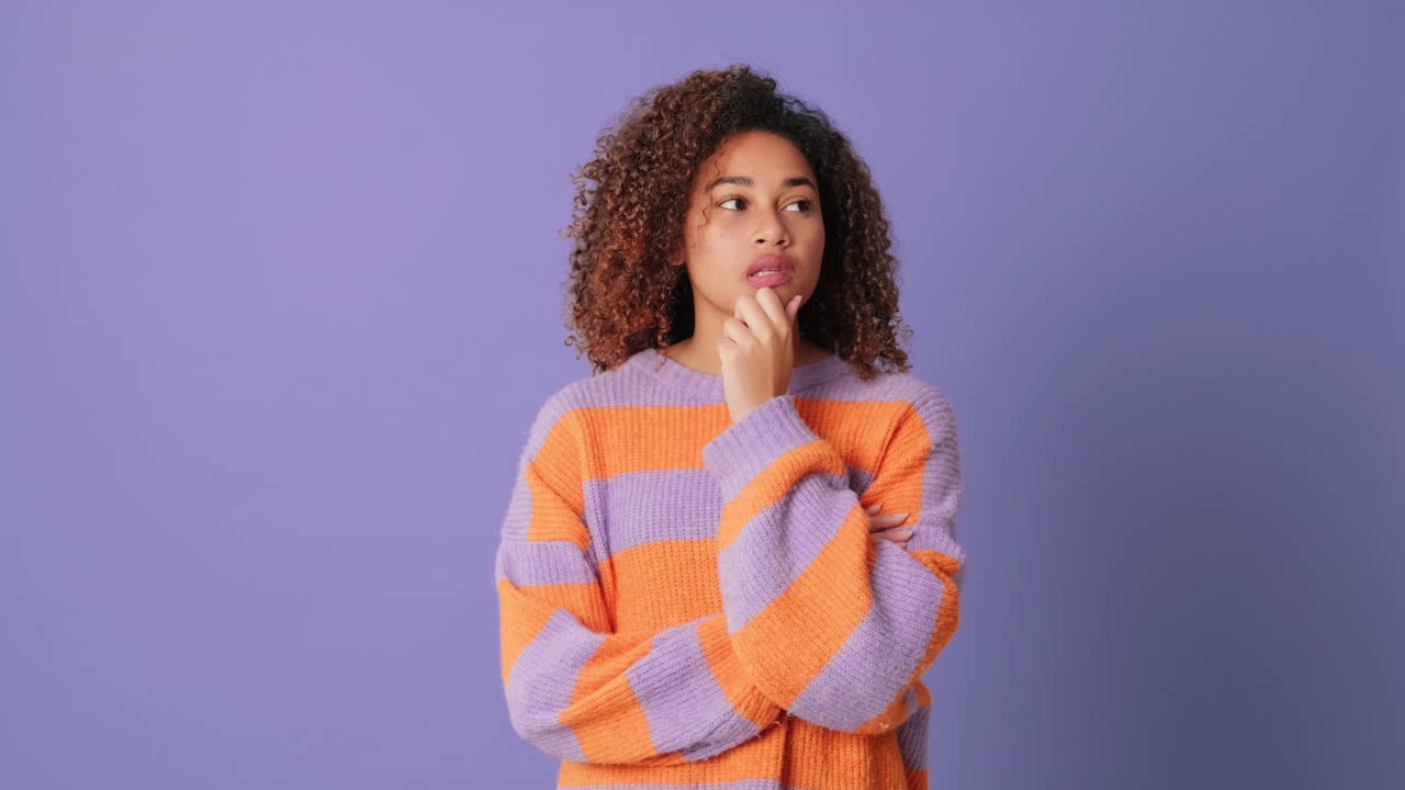 Pensive Young Woman with Curly Hair Thinking on Purple Background