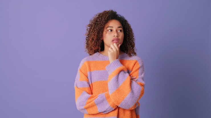 Pensive Young Woman with Curly Hair Thinking on Purple Background
