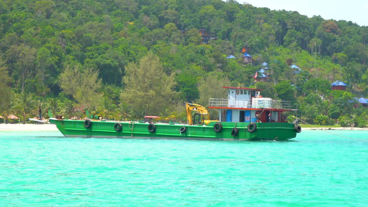 배경에 섬과 나무가 있는 캄보디아 해변에 정박한 녹색 건설 바지선