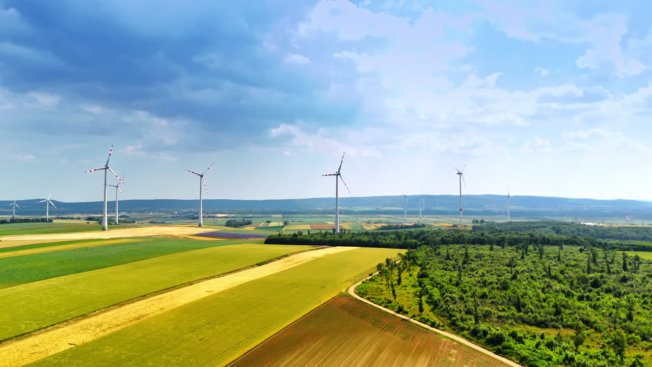 Flight over the fields in the countryside on summer day. Wind mills rotate in the wind producing green energy