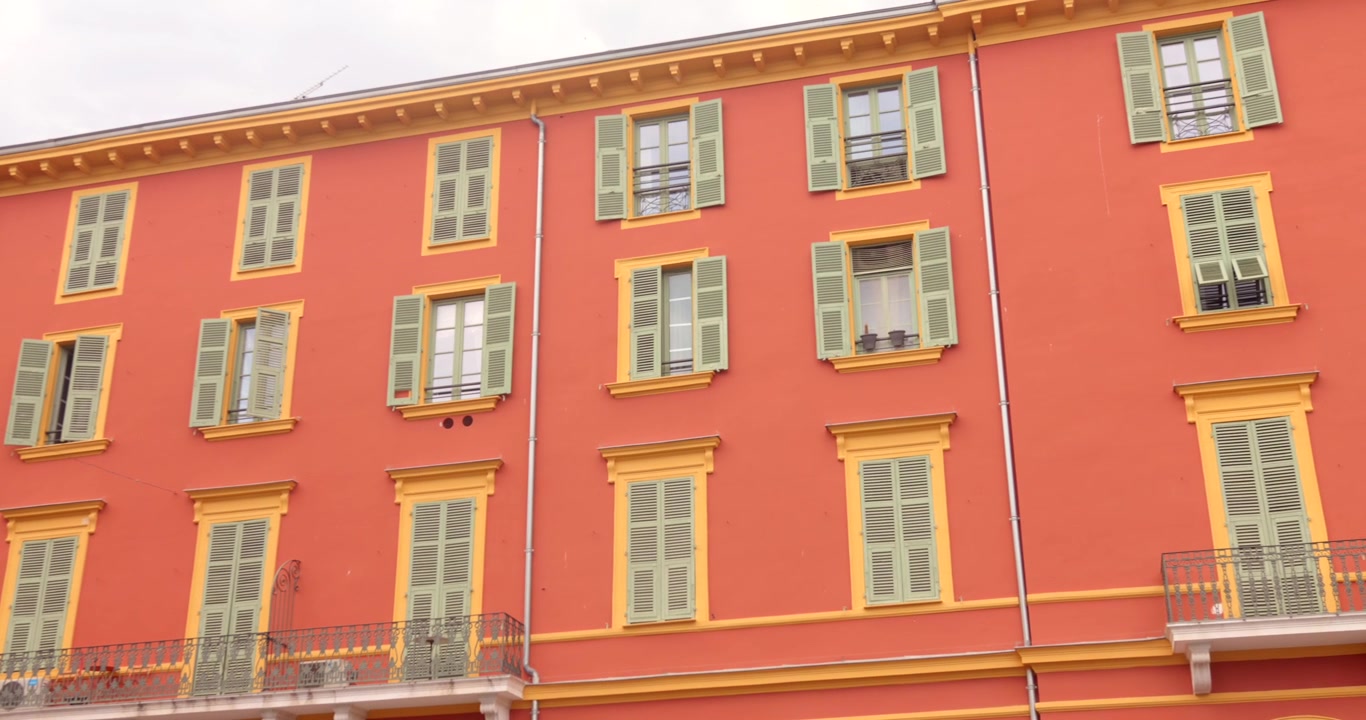 Fachada colorida de edifício histórico em vermelho e amarelo com janelas tradicionais com persianas em Nice, França, na ensolarada Riviera Francesa.