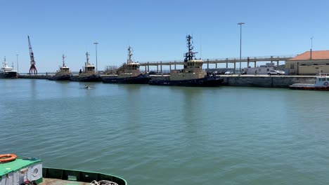 a-couple-of-lovers-canoeing-in-the-sea-port-of-alcantara-on-a-sunny-day-with-some-armed-forces-ships-in-the-background