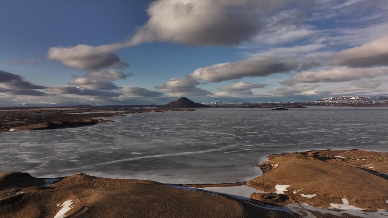 Wide-angle aerial of Lake Mývatn's icy surface with volcanic hills and distant clouds near Skútustaðir. Iceland