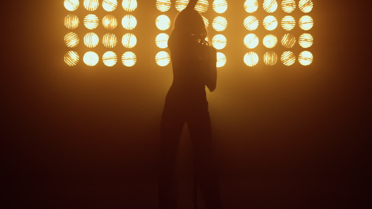 silueta de una mujer cantando bailando sensualmente cerca del micrófono en las luces del estudio.