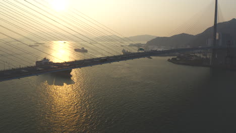 Buque-Portacontenedores-Acercándose-Al-Puerto-De-Hong-Kong-Detrás-Del-Puente-Colgante-Durante-La-Hora-Dorada