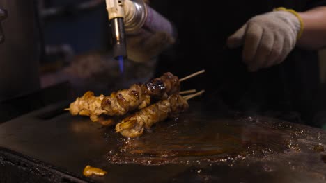 chef cooking skewered meat with a blowtorch