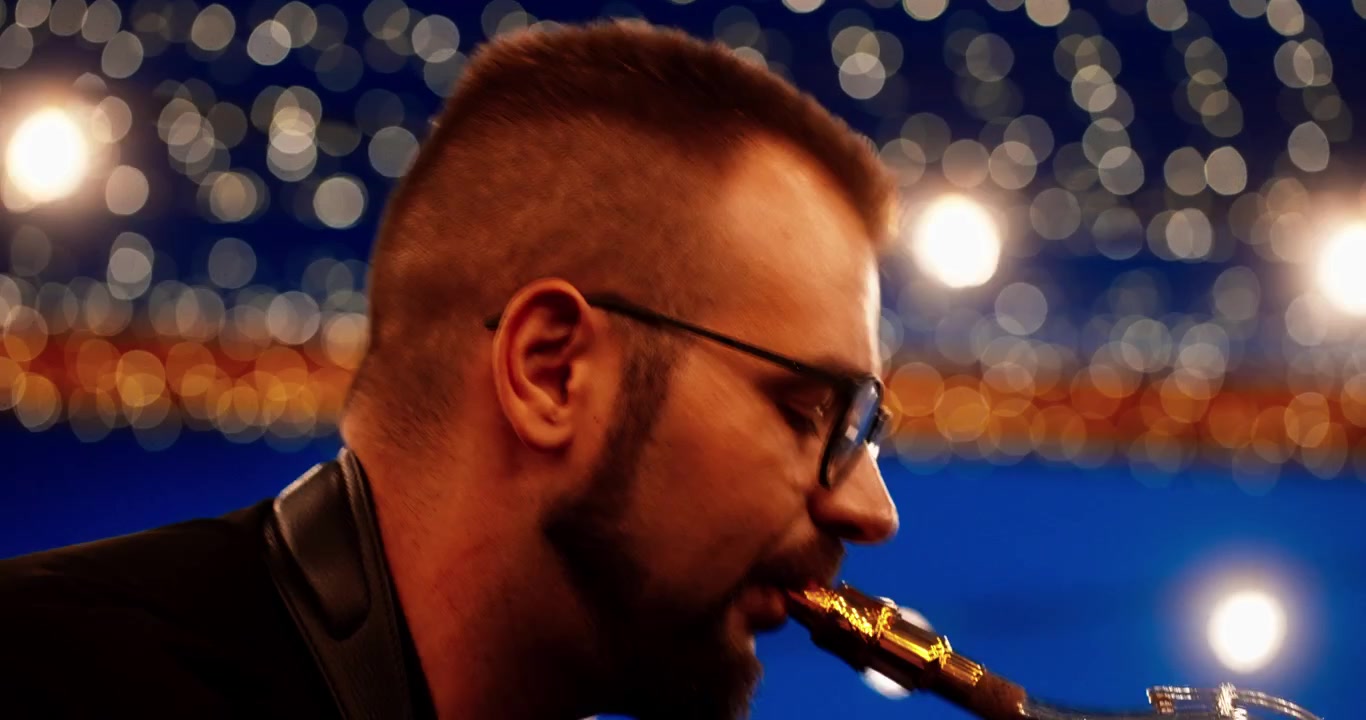 Musicista che suona un sassofono argentato sul palco con luci bokeh
