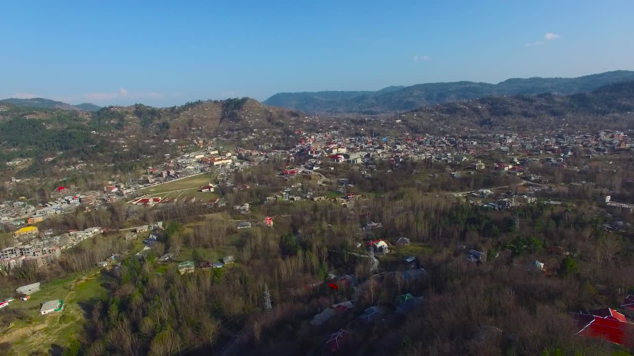 Drone shot of a beautiful village with beautiful houses, trees, hills and blue sky.