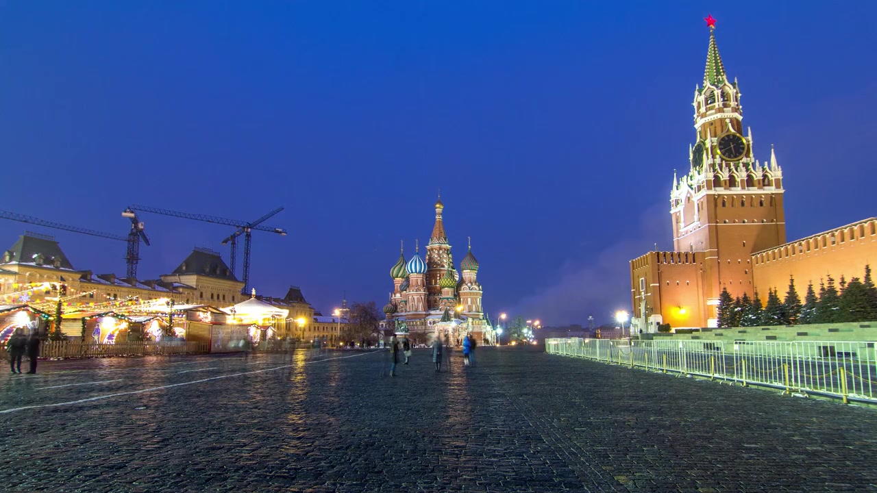 Timelapse de la Place Rouge à Moscou, pendant la transition du jour à la nuit. Le Kremlin de Moscou avec l'emblématique Tour Spasskaïa et la Cathédrale Saint-Basile sont illuminés, créant une scène époustouflante.
